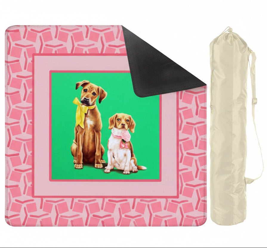 Pink patterned picnic blanket with two dogs on a green background, accompanied by a black carrying bag.