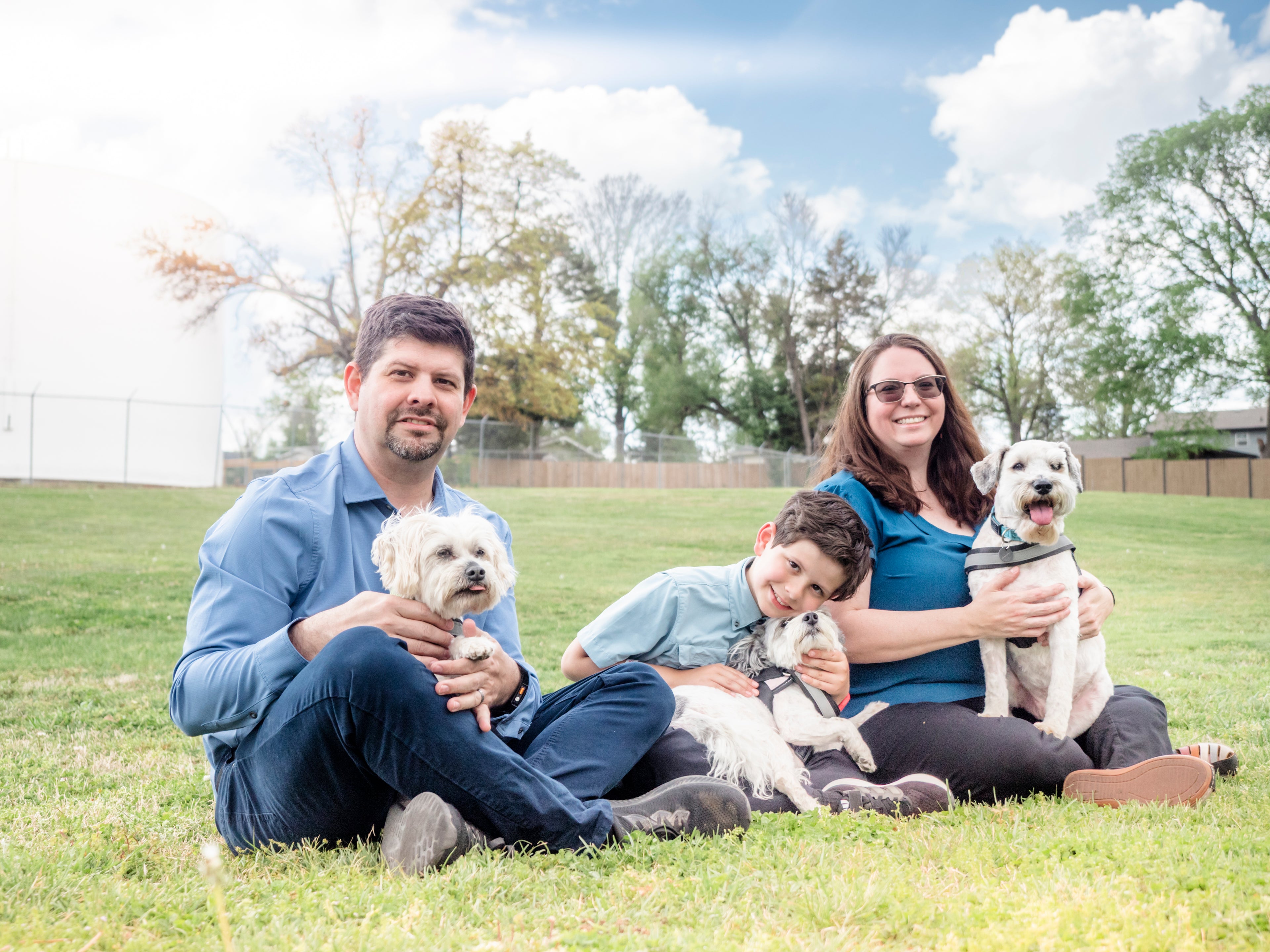 Family of three with three dogs sitting on a grassy field.