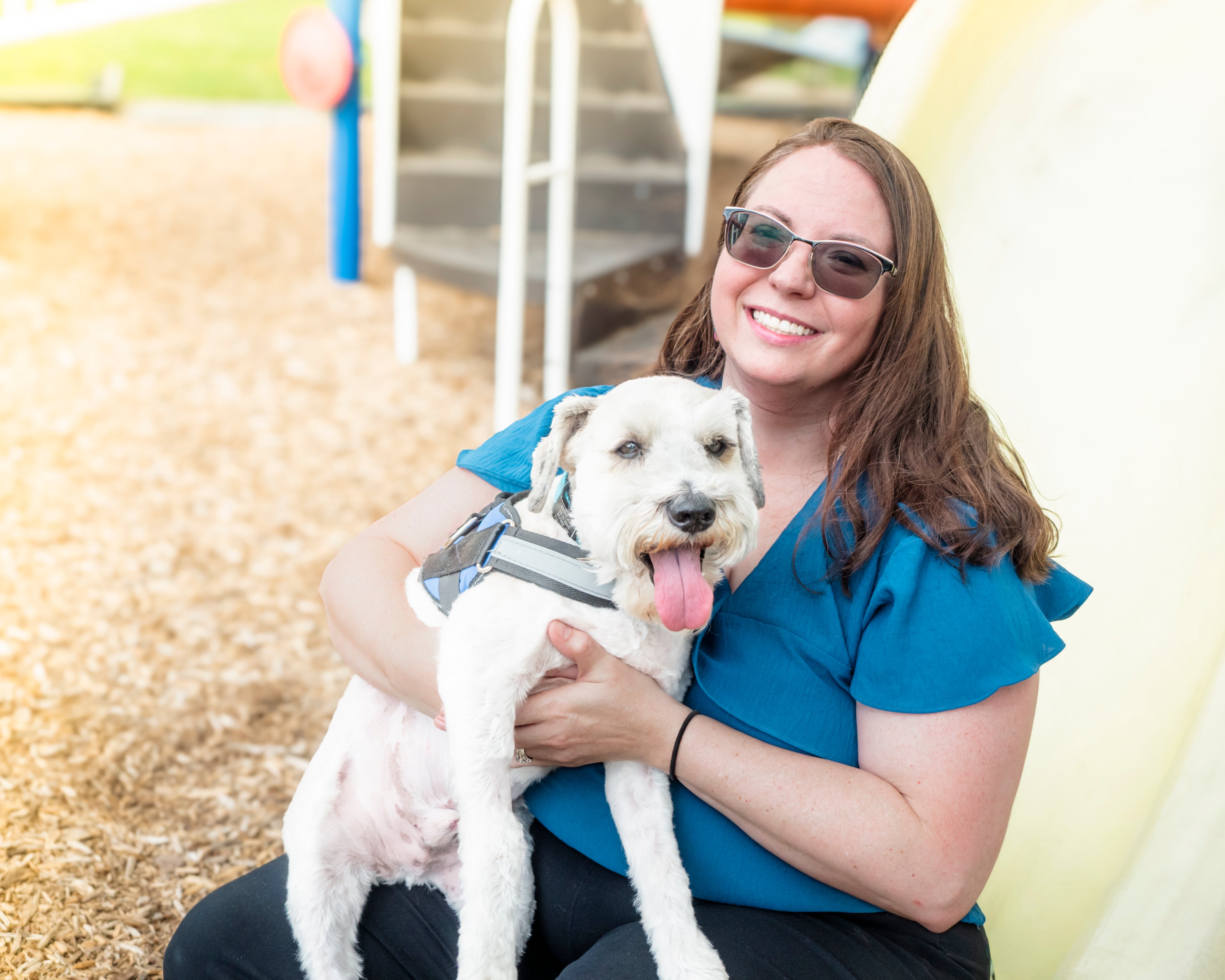 Woman holding a dog in an outdoor setting with playground equipment in the background